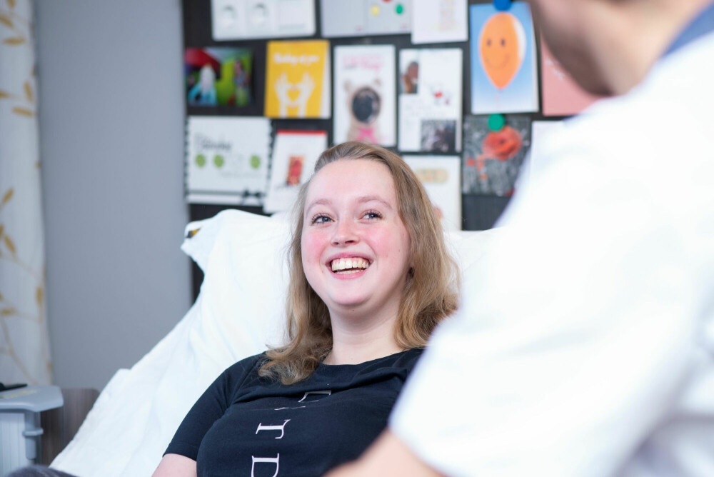 Romy ligt in haar bed op de kliniek van Vogellanden. Een verpleger zit naast haar
