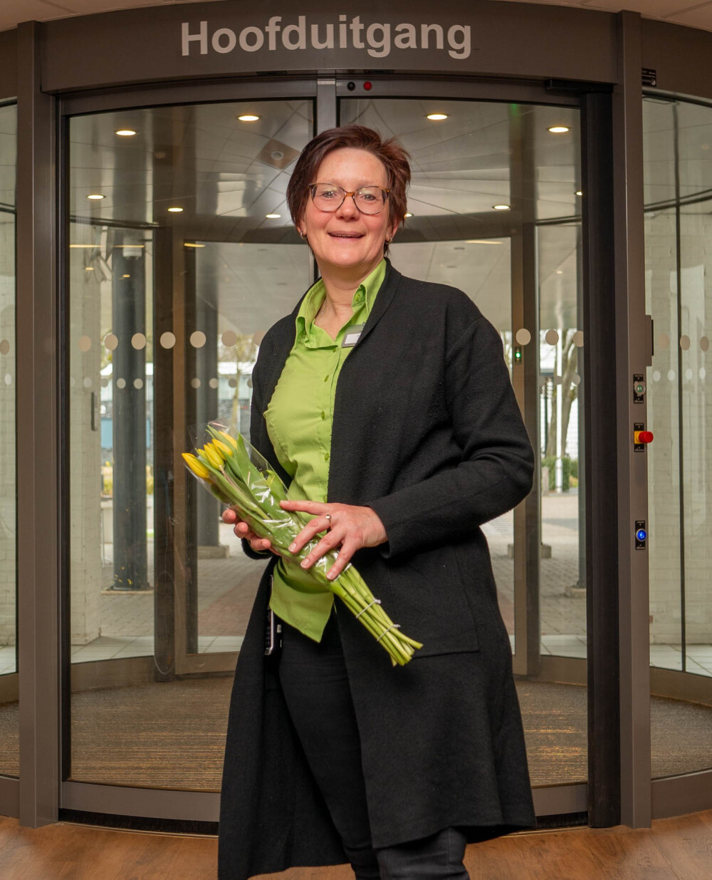 Gastvrouw Marijke staat voor de ingang van Vogellanden met een bos bloemen in haar handen