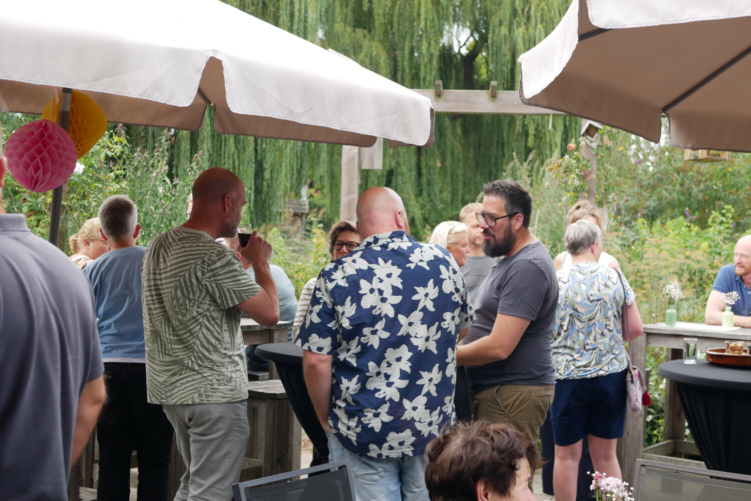 Groep buurtbewoners en medewerkers praten met elkaar met een drankje in hun hand
