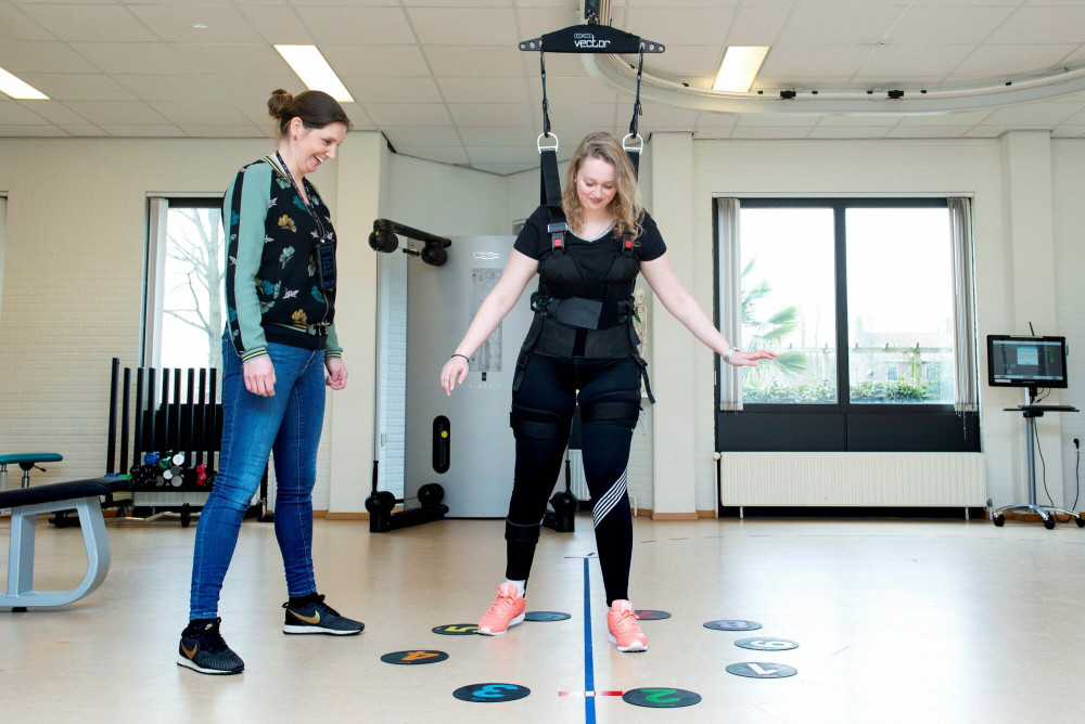 Behandelaar en patiënt doen loopoefeningen m.b.v. bodyweightsysteem