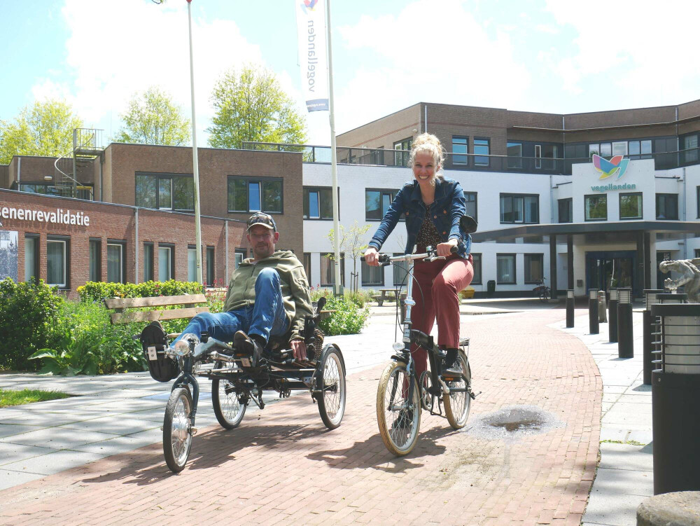 Ergotherapeut fietst met patiënt met aangepaste fiets