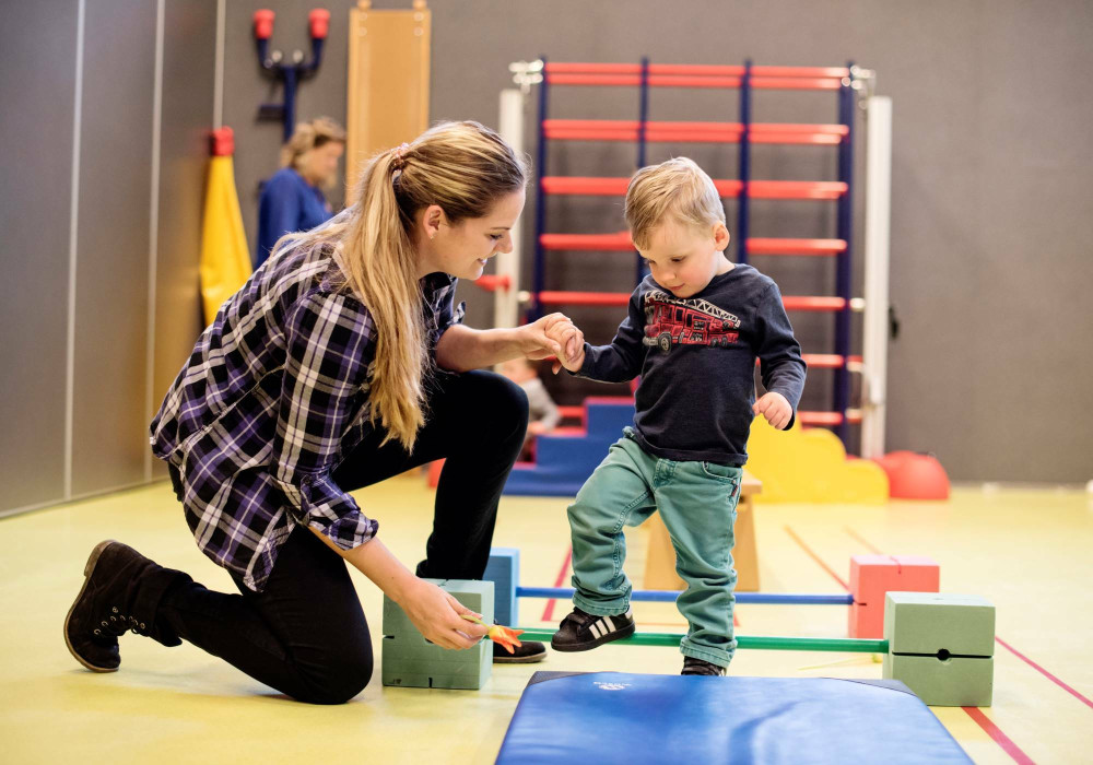 Kind met behandelaar in sportzaal kinderrevalidatie