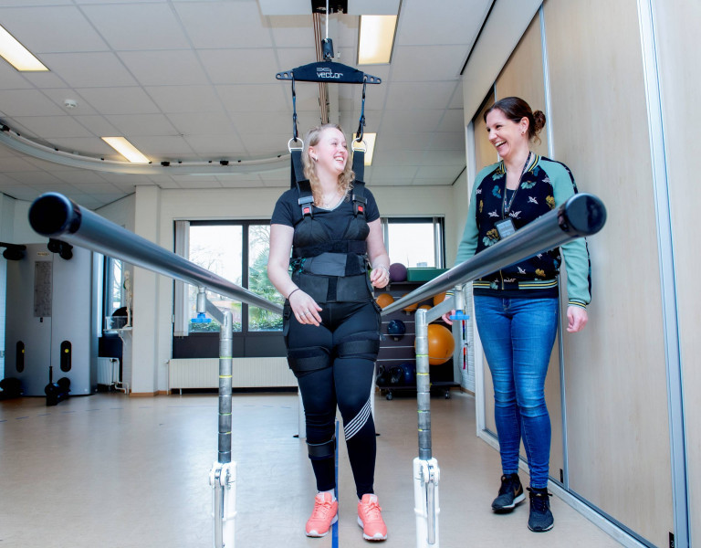 Behandelaar en patiënt doen loopoefeningen m.b.v. bodyweight support system bij loopbrug