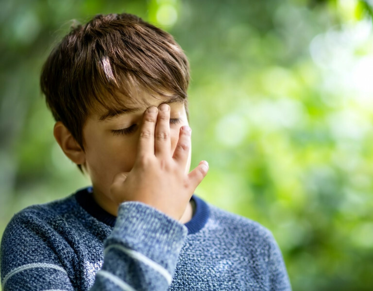 Jongen met een niet-aangeboren hersenletsel heeft zijn hand aan zijn gezicht